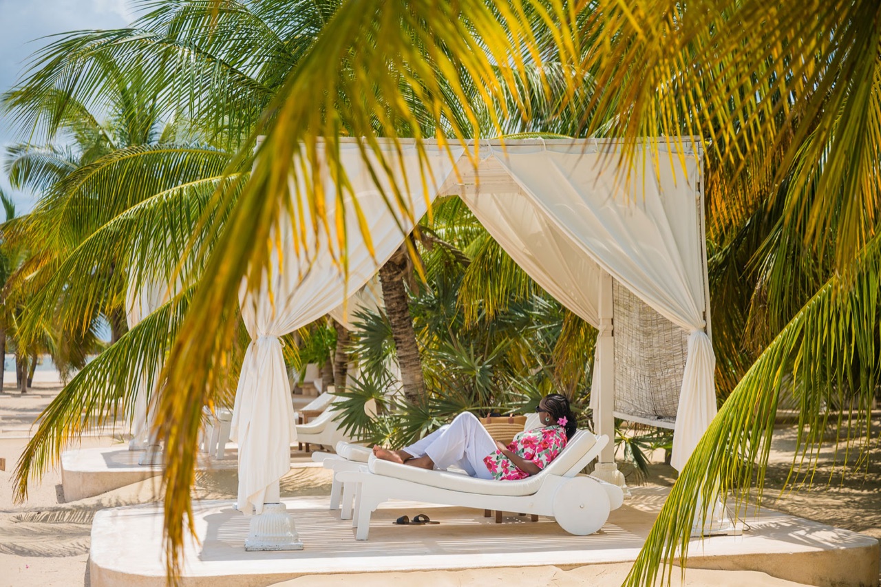 A couple relaxing under a canopy daybed on the beach at The Majlis
